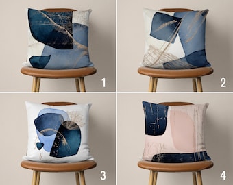 Può includere: Quattro cuscini decorativi con motivi astratti in tonalità di blu, oro e rosa. I cuscini sono su sedie marroni con gambe in legno.