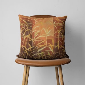 Puede incluir: Una almohada de color marr&oacute;n y naranja con un patr&oacute;n geom&eacute;trico de plantas estilizadas. La almohada est&aacute; sentada en una silla de cuero marr&oacute;n.