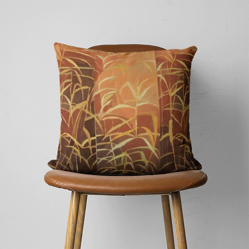 Puede incluir: Una almohada de color marr&oacute;n y naranja con un patr&oacute;n geom&eacute;trico de plantas estilizadas. La almohada est&aacute; sentada en una silla de cuero marr&oacute;n.