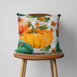May include: A white throw pillow with a watercolor design of pumpkins and vines. The pumpkins are orange, green, and yellow. The vines are green and have small orange flowers.