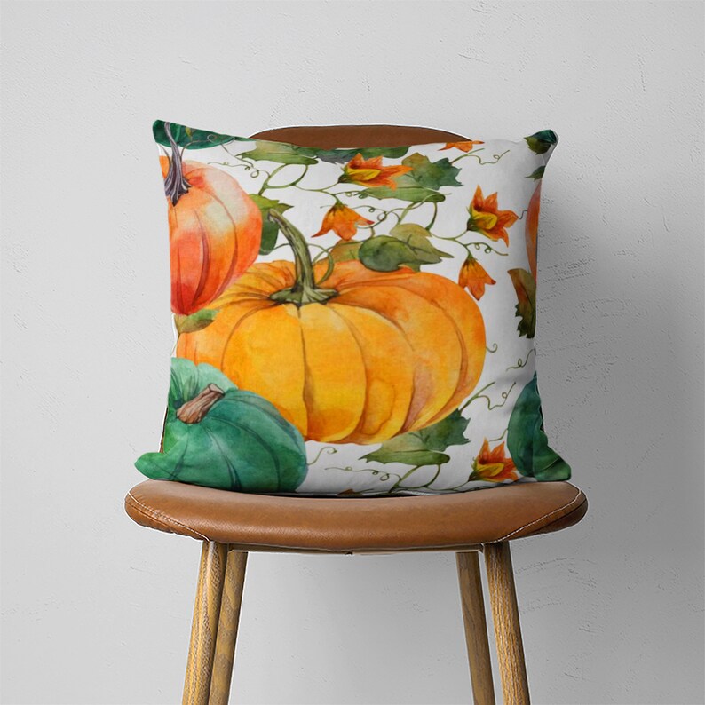 May include: A white throw pillow with a watercolor design of pumpkins and vines. The pumpkins are orange, green, and yellow. The vines are green and have small orange flowers.