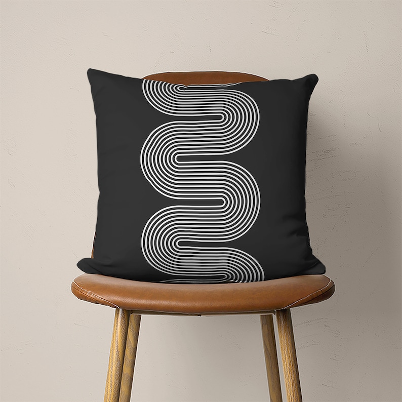 May include: Black and white geometric pillow with a wavy line pattern. The pillow is sitting on a brown chair.