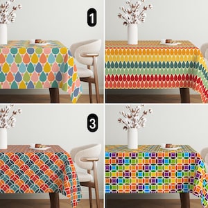 Op de afbeelding: Vier verschillende tafelkleden met geometrische patronen in verschillende kleuren, waaronder rood, geel, blauw, groen en oranje. De tafelkleden worden getoond op een tafel met een witte stoel.