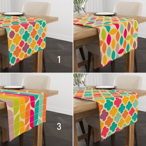 Op de afbeelding: Vier kleurrijke tafellopers met geometrische patronen worden getoond op houten tafels. Elke loper heeft een ander ontwerp, waaronder bloem- en abstracte vormen in levendige kleuren zoals oranje, roze, groen en blauw. De lopers liggen op tafels met borden en stoelen.