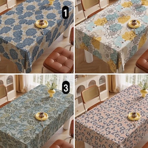 May include: Four rectangular tablecloths with floral patterns are displayed. The tablecloths feature different color schemes: blue and white, yellow and blue, green and white, and pink and navy. Each tablecloth is set on a table with a small plate and a vase.