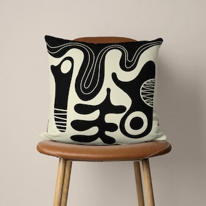 Puede incluir: Una almohada con un dise&ntilde;o abstracto en blanco y negro sobre un fondo crema. El dise&ntilde;o presenta formas y l&iacute;neas org&aacute;nicas.