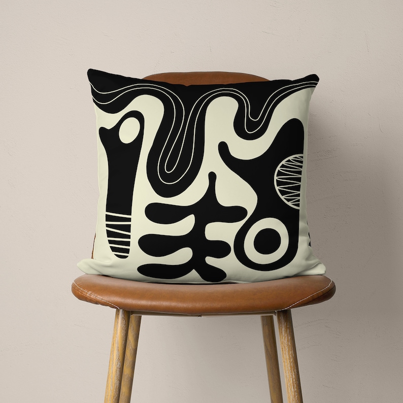 Puede incluir: Una almohada con un dise&ntilde;o abstracto en blanco y negro sobre un fondo crema. El dise&ntilde;o presenta formas y l&iacute;neas org&aacute;nicas.