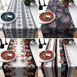 Op de afbeelding: Vier tafelrunners met verschillende nautische ontwerpen. De runners zijn allemaal wit met blauwe en rode accenten. De ontwerpen omvatten ankers, strepen, schelpen en koraal.