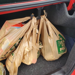 May include: A car trunk with several brown grocery bags hanging from a black hook. The bags are filled with groceries and have green labels with the text "DONATED BY" and "OVER 1 MILLION" on them.