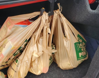 May include: A car boot with several brown grocery bags hanging from a black hook. The bags are filled with groceries and have green labels with the text "DONATED BY" and "OVER 1 MILLION" on them.