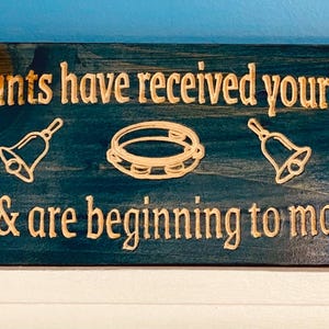 May include: A teal blue wooden sign with the text "The happy haunts have received your sympathetic vibrations & are beginning to materialize." in gold lettering. The sign also features two gold bells and a gold tambourine.
