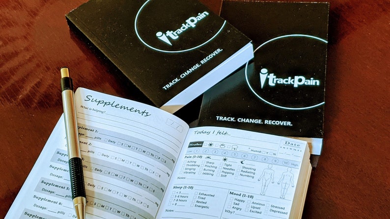 May include: Two black notebooks with the text "iTrackPain" and "TRACK. CHANGE. RECOVER." on the covers. One notebook is open to a page with a section for tracking supplements and another section for tracking pain, sleep, and mood.