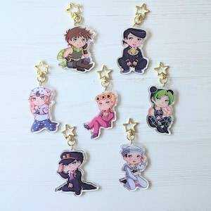 Op de afbeelding: Zeven kleurrijke anime-personage sleutelhangers met gouden ster bedels. De personages zijn afgebeeld in een chibi-stijl en dragen verschillende outfits.