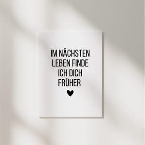 May include: A white rectangular print with black text that reads "IM N&Auml;CHSTEN LEBEN FINDE ICH DICH FR&Uuml;HER" and a black heart symbol. The print is centered on a white background.