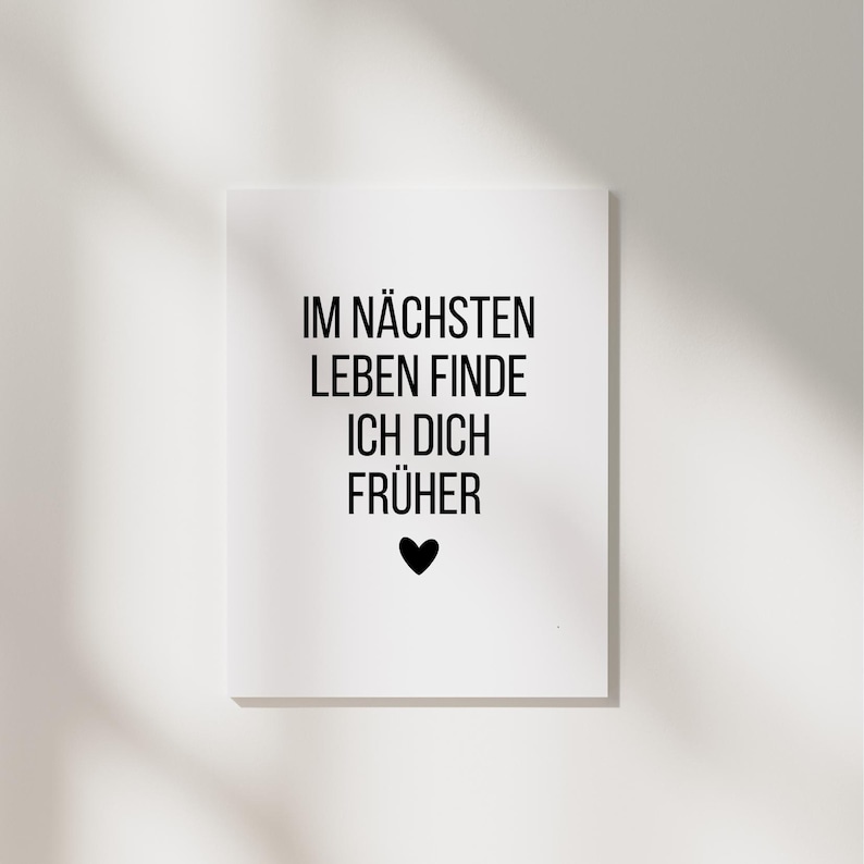 May include: A white rectangular print with black text that reads "IM N&Auml;CHSTEN LEBEN FINDE ICH DICH FR&Uuml;HER" and a black heart symbol. The print is centered on a white background.