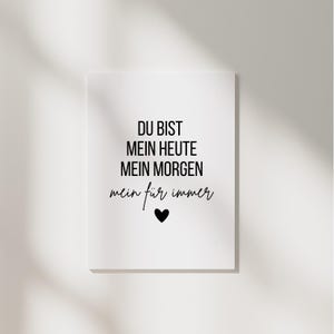 Könnte beinhalten: Eine weiße rechteckige Leinwand mit schwarzem Text, der lautet: "DU BIST MEIN HEUTE MEIN MORGEN mein für immer" mit einem schwarzen Herzsymbol. Die Leinwand wird vor einer weißen Wand mit Schatten angezeigt.