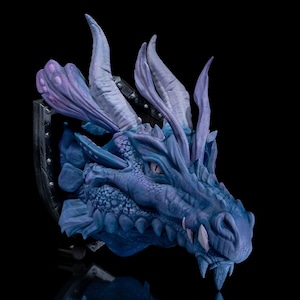May include: A blue and purple dragon head sculpture with intricate details, mounted on a shield-shaped base. The dragon has a fierce expression with sharp teeth and a textured, scaly skin.