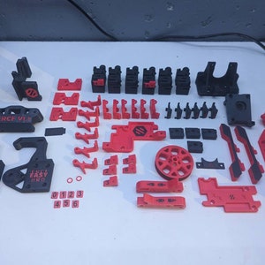 May include: A collection of 3D printed parts in black and red. The parts include a variety of shapes and sizes, including gears, wheels, and brackets. The parts are labeled with the text "ERCF V1.8" and "Easy Pro".