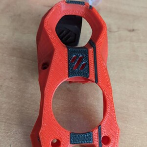 May include: A 3D printed red plastic part with black accents. The part has a textured surface and two holes.