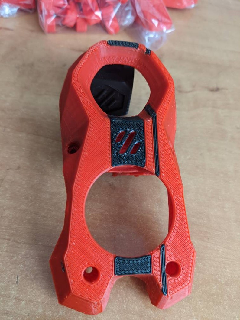 May include: A 3D printed red plastic part with black accents. The part has a textured surface and two holes.
