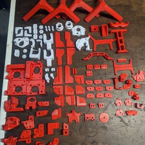 Puede incluir: Una colecci&oacute;n de piezas impresas en 3D en rojo y blanco. Las piezas son de varias formas y tama&ntilde;os, y algunas tienen agujeros o ranuras. Las piezas probablemente sean para un proyecto de impresi&oacute;n 3D.