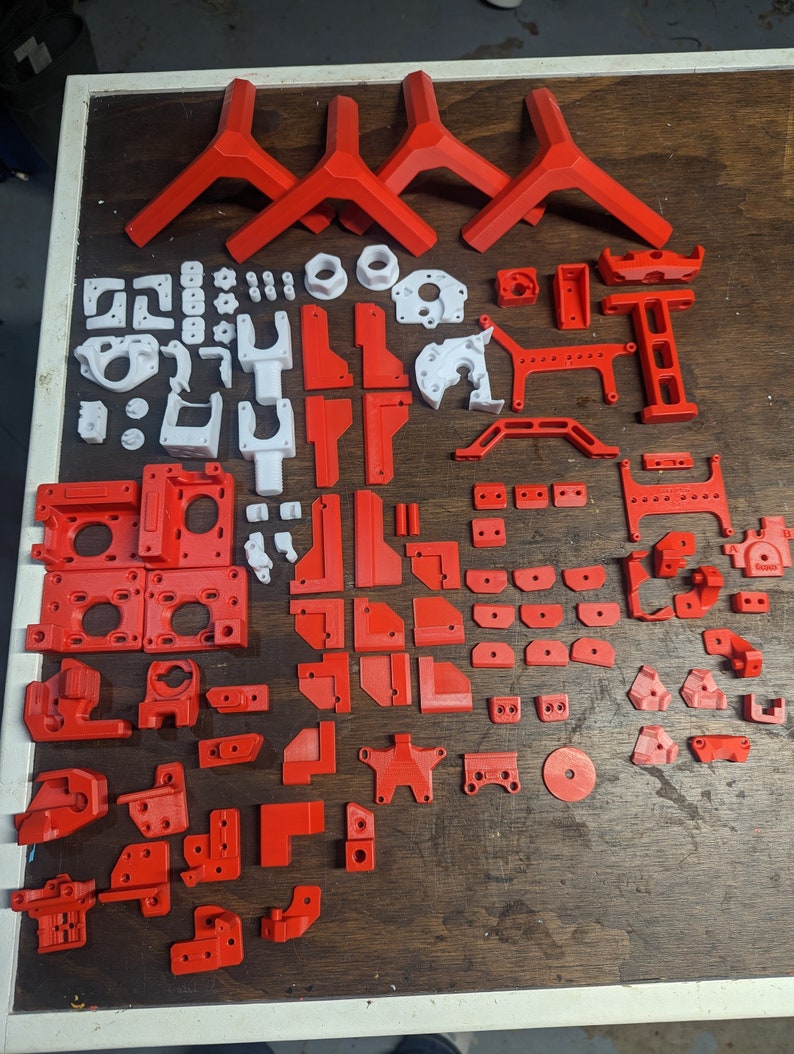 Puede incluir: Una colecci&oacute;n de piezas impresas en 3D en rojo y blanco. Las piezas son de varias formas y tama&ntilde;os, y algunas tienen agujeros o ranuras. Las piezas probablemente sean para un proyecto de impresi&oacute;n 3D.