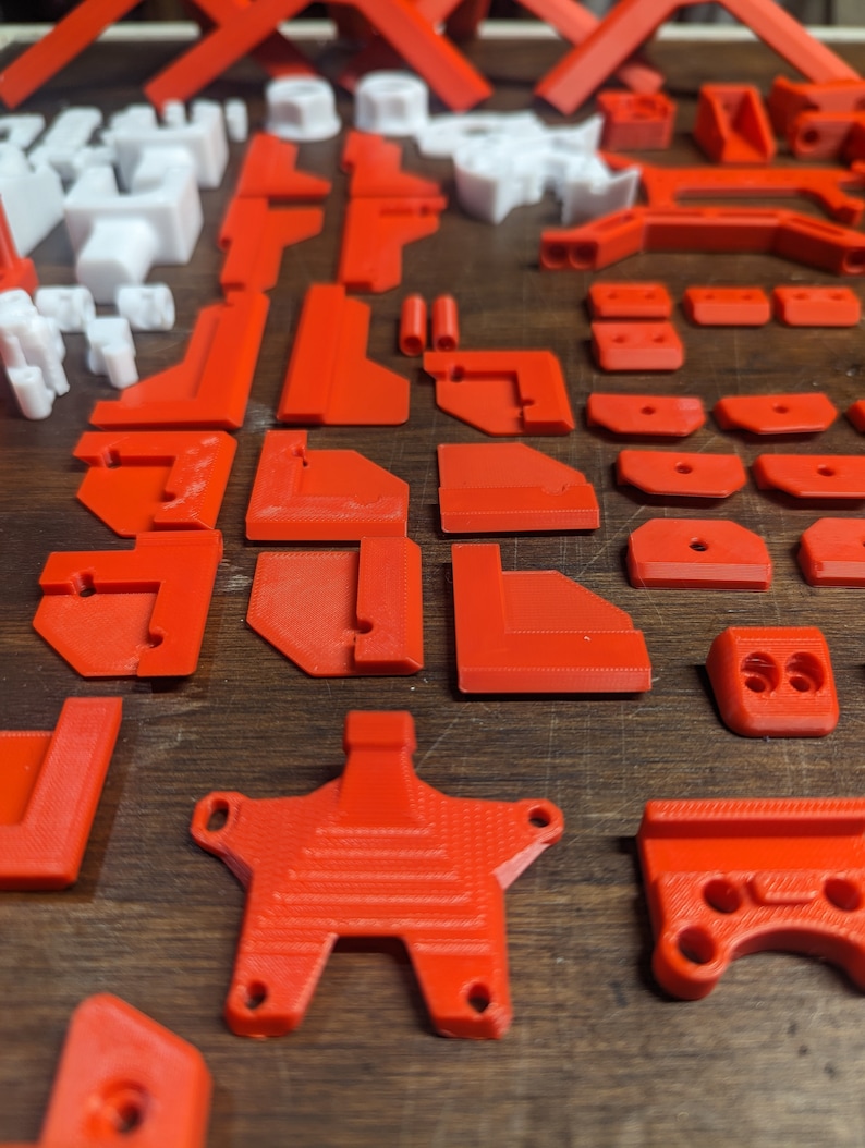 Puede incluir: Una colecci&oacute;n de piezas de pl&aacute;stico rojo impresas en 3D, que incluyen varias formas y tama&ntilde;os, como esquinas, conectores y una pieza en forma de estrella. Las piezas est&aacute;n dispuestas sobre una superficie de madera.