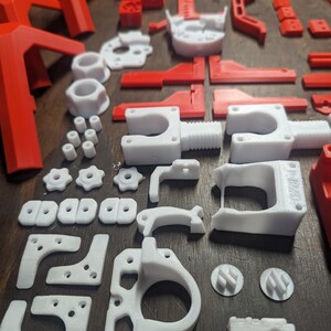 Puede incluir: Una colecci&oacute;n de piezas impresas en 3D en pl&aacute;stico blanco y rojo. Las piezas incluyen engranajes, soportes y otros componentes.