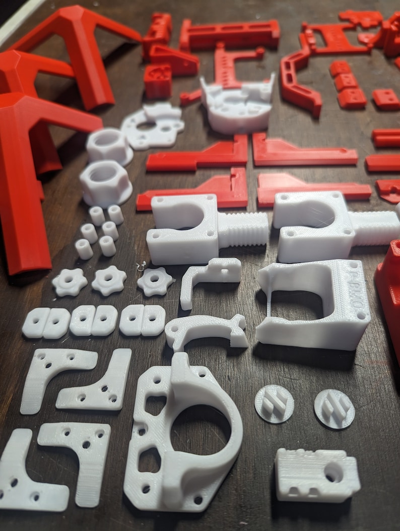 Puede incluir: Una colecci&oacute;n de piezas impresas en 3D en pl&aacute;stico blanco y rojo. Las piezas incluyen engranajes, soportes y otros componentes.