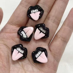 May include: Five black resin mouth charms with pink tongues sticking out. The charms are about 1 inch in diameter.
