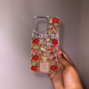 Puede incluir: Una funda de tel&eacute;fono transparente con un fondo de purpurina dorada y labios rojos, una jeringa y un dise&ntilde;o de frasco de perfume. El texto "INJECTOR KIM" est&aacute; escrito en la funda.