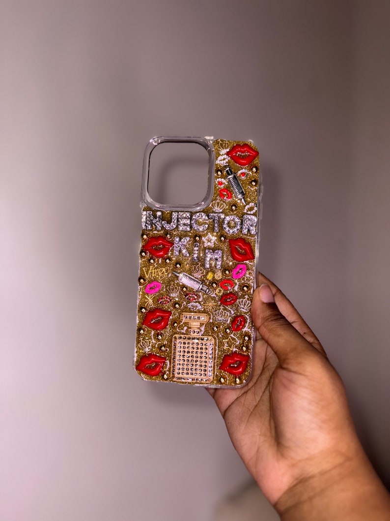 Puede incluir: Una funda de tel&eacute;fono transparente con un fondo de purpurina dorada y labios rojos, una jeringa y un dise&ntilde;o de frasco de perfume. El texto "INJECTOR KIM" est&aacute; escrito en la funda.