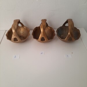 Może przedstawiać: Trzy małe, złote, ozdobne koszyki z zakręconymi uchwytami. Koszyki są ułożone w rzędzie od lewej do prawej. Każdy kosz ma numer napisany na białym kawałku papieru pod spodem.