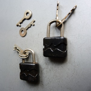May include: Two black padlocks with keys. One padlock has three keys attached to it. The padlocks have a wavy design.