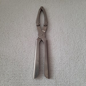 Puede incluir: Un cascanueces de plata con un borde dentado y un mango que dice "Inglaterra".