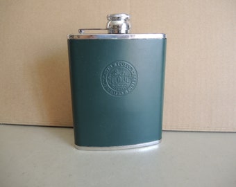 Puede incluir: Una petaca de metal verde con tapa plateada y un sello plateado en relieve que dice "The Scotch Malt Whisky Society".