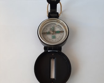 May include: A black compass with a silver face and a green arrow pointing north. The compass has a folding lid and a loop for attaching to a keychain.