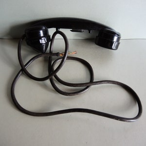 Könnte beinhalten: Ein schwarzes Vintage-Drehwahltelefon-Handset mit einem Spiralkabel.