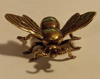 May include: A gold-colored metal bee figurine with green accents. The bee has detailed wings and legs.