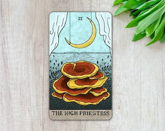May include: The High Priestess tarot card features a crescent moon and a stack of red and yellow mushrooms against a blue and green background.