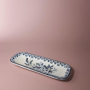 Peut inclure: Plat rectangulaire avec une base blanche et un motif floral bleu. Le plat a une bordure bleu foncé et mesure environ 30 cm de long.