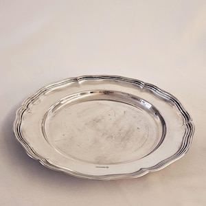 May include: Oval silver serving platter with a scalloped edge. The platter has a polished finish and a simple, elegant design. The rim features a subtle, repeating pattern. A classic piece for serving food.