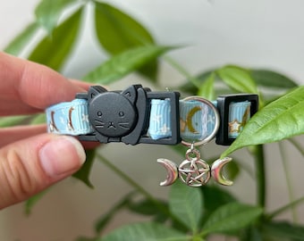 May include: A blue cat collar with a black cat charm and a silver charm with a triple moon and pentacle design. The collar is decorated with gold stars and crescent moons.