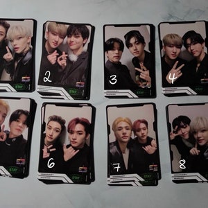 Könnte beinhalten: Acht Foto-Karten mit einer K-Pop-Boyband. Die Karten sind schwarz-weiß mit einem grün-weißen Logo, auf dem "STAY" und "ODDINARY" in weißer Schrift stehen. Jede Karte hat eine Nummer von 1 bis 8, die in weiß auf die Karte geschrieben ist. Die Bandmitglieder tragen schwarze Kleidung und posieren für die Kamera.