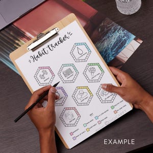 May include: A wooden clipboard with a printed habit tracker sheet. The sheet features hexagonal boxes with icons for workout, water intake, reading, healthy food, and more. The words "Habit Tracker" are at the top. A hand is holding a pen.