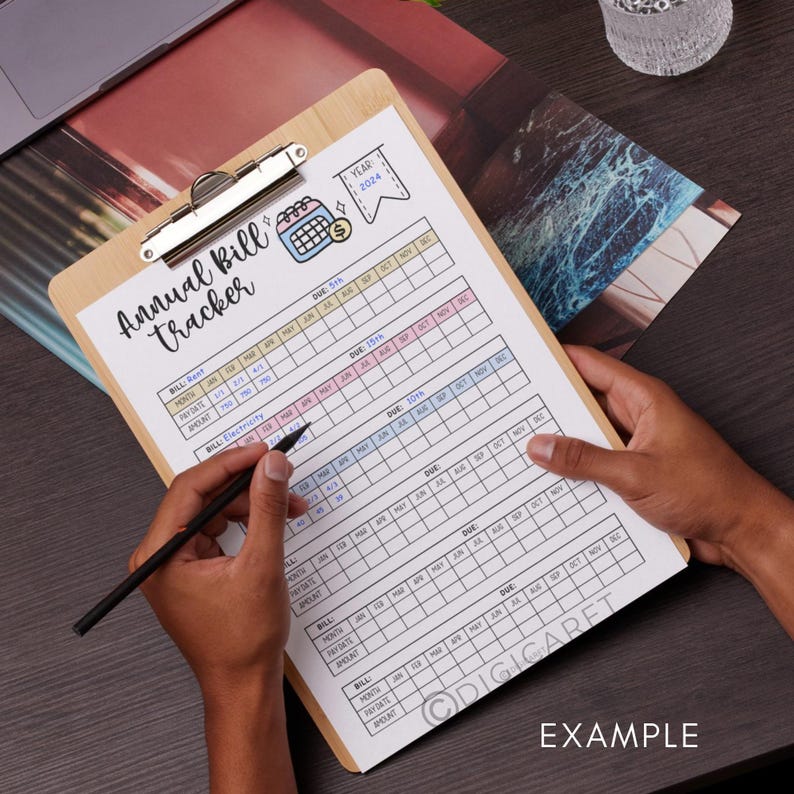 May include: A printable annual bill tracker on a clipboard with a hand holding a pen. The tracker has a calendar layout with columns for each month of the year and rows for different bills, such as rent, electricity, and internet. The tracker is labeled "Annual Bill Tracker" and "Year: 2024".