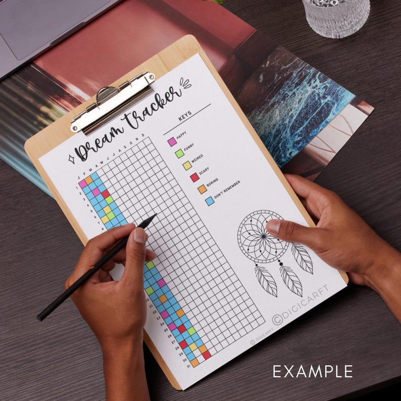 May include: A white dream tracker with a grid for logging dreams each month. The grid is colour-coded with keys for happy, funny, weird, scary, boring, and don't remember. A dreamcatcher illustration is at the bottom of the page. The text "Dream Tracker" and "Keys" are at the top of the page. The text "EXAMPLE" is at the bottom of the page.