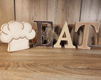 EAT! Distressed, free standing wood letters for kitchen decor in warm browns and coordinating chef hat. Three styles to choose from.