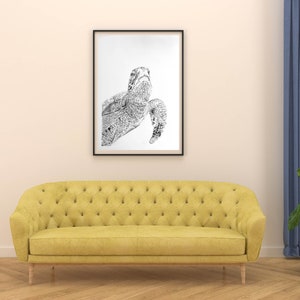 May include: A black and white line drawing of a sea turtle in a black frame hanging above a yellow tufted sofa in a living room setting.