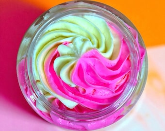 May include: A jar filled with a swirl of pink and light green cream. The cream is arranged in a spiral pattern, with the colors blending together. The jar is clear, and the background is a gradient of pink and orange.